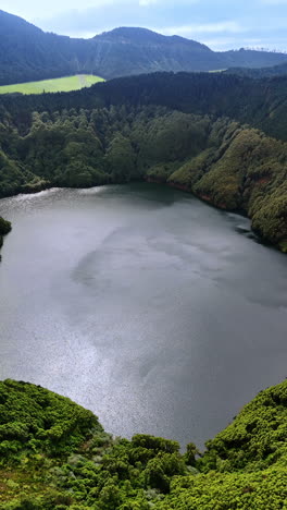 beautiful small lake inside the mountain overgrown with lush greenery. stunning nature of the azorean islands from top view. vertical video.