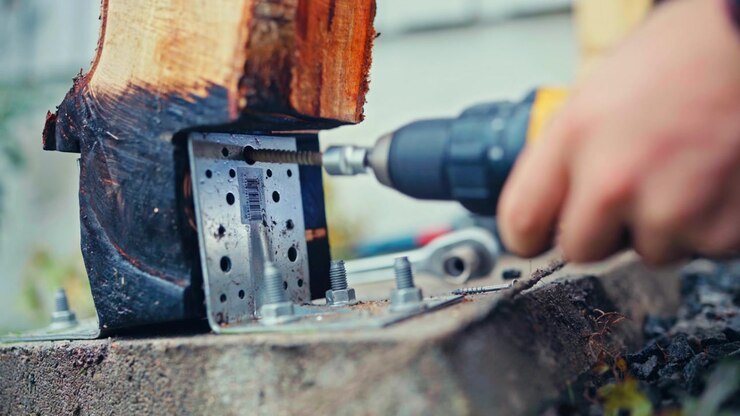 A Power Drill Driving a Screw Into a Wooden Post Secured by a Metal Bracket and Bolts, Highlighting Construction and Fastening Work During an Outdoor Building Project - Close-Up Shot