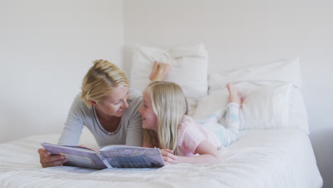 side view of a caucasian woman reading a story to her daughter on bed