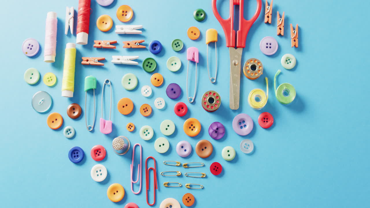 video de tijeras, botones, alfileres, clips, clavijas y bobinas de algodón en forma de corazón sobre fondo azul