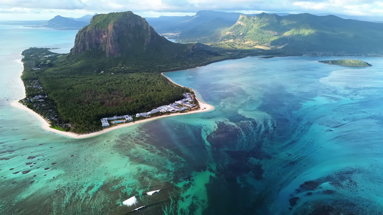 Vista aérea con dron de la península de Le Morne Brabant en Mauricio, mostrando arrecifes de coral, aguas turquesas de la laguna y la icónica montaña elevándose sobre la costa tropical.