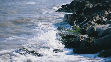 The-sea-waves-crash-into-a-rocky-seashore-with-green-moss