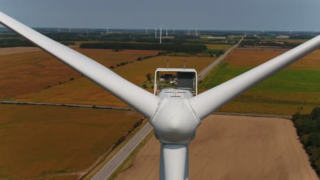 wind turbine close up of nose cone and propellers with farmland in the background, aerial drone shot