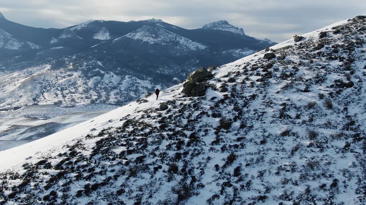 백커가 산의 풍경을 배경으로 눈으로 인 언덕의 경사에서 고 있습니다.