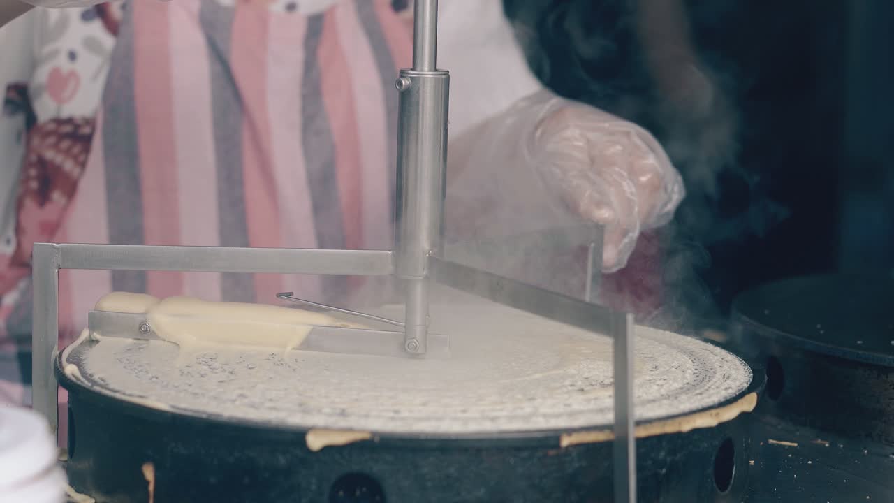 повар в перчатках распространяет тесто над креппером в кафе