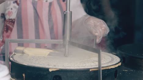 cocinero con guantes extiende la masa sobre el fabricante de crepes en el café
