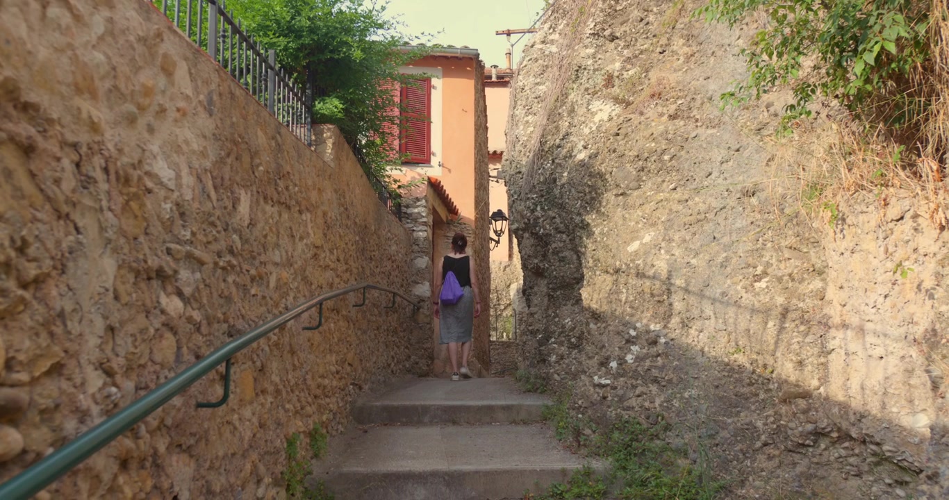 Woman walking up stone steps in a charming, narrow alleyway of the historic medieval village of Roquebrune-Cap-Martin, French Riviera. Scenic stroll in a picturesque, old-fashioned European setting, t