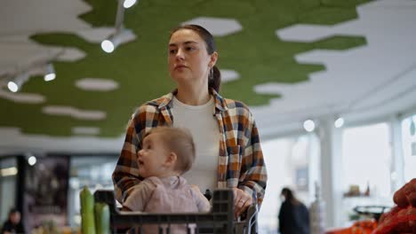 Confident-brunette-girl-in-a-plaid-shirt,-mother-of-a-little-girl-shopping-with-her-daughter-in-the-supermarket