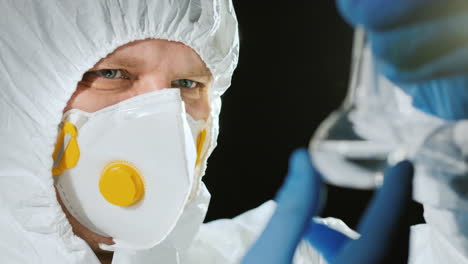 scientist in protective suit looks at a test tube with a transparent drug