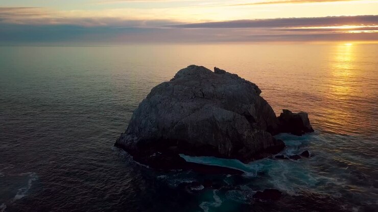 Lenta orbita al tramonto attorno a un'enorme roccia oceanica e onde che si infrangono a Sand Dollar Beach a Big Sur, California