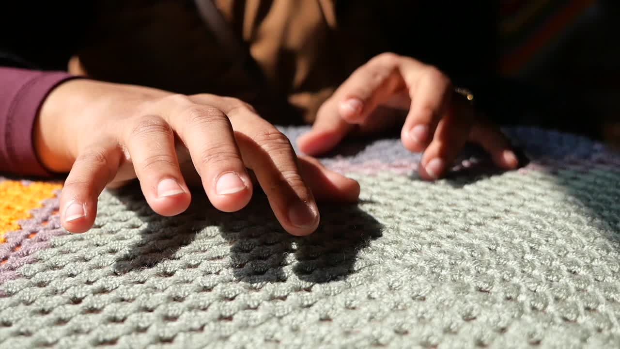 Close-up of hands resting on a knitted blanket