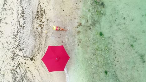 aerial top view of woman sunbathing by umbrella on seashore, dolly in