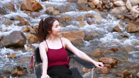 asian woman in red sitting on a chair with big rocks and water slow splashing for relaxing and happiness in the vacation summertime