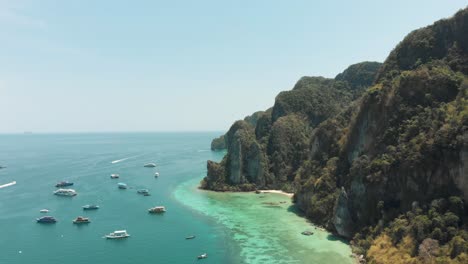 towering limestone stalled by shoreline winding around ko phi phi don island paradise, thailand - aerial fly-over shot