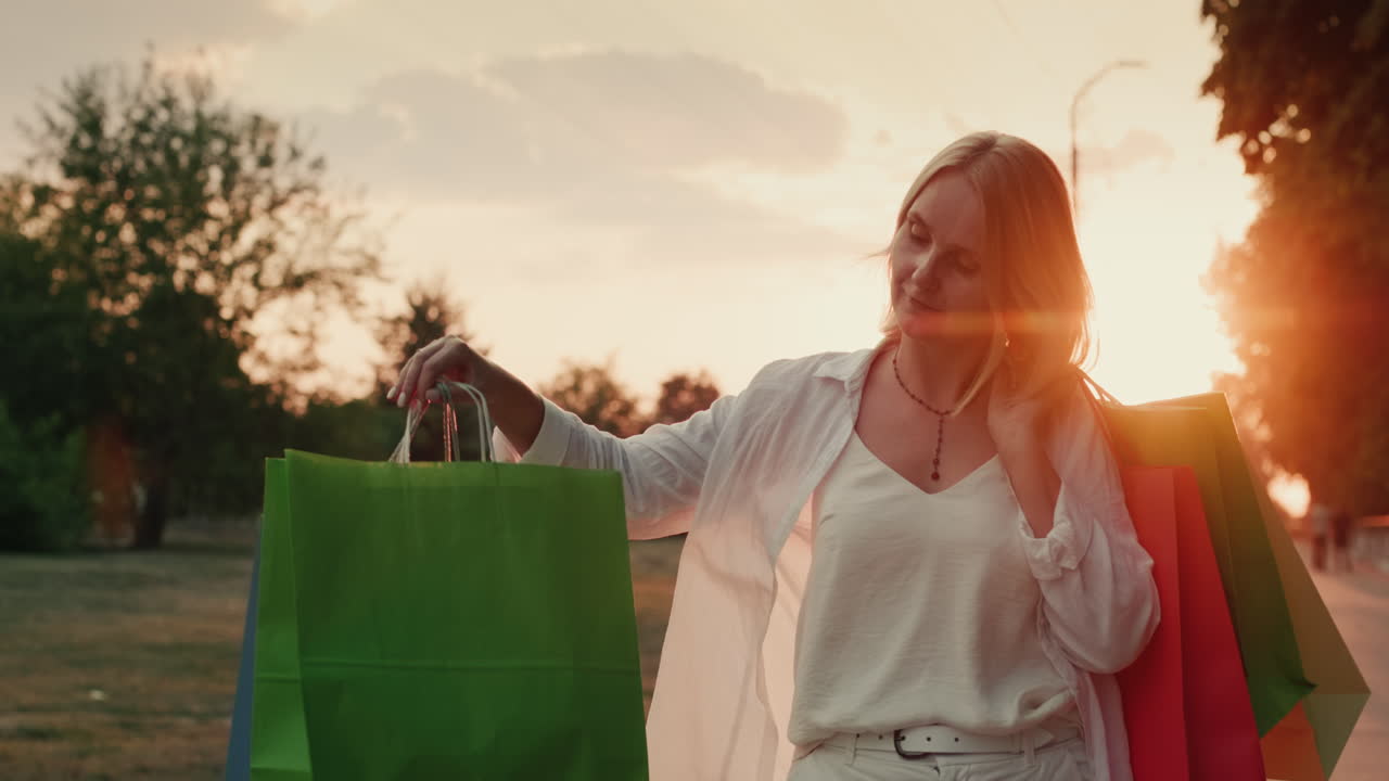 패키지가 있는 쇼핑객이 일몰 2에 길을 걸어갑니다.