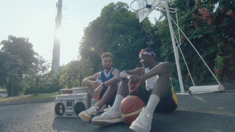 two friends resting with ghetto blaster and chatting on basketball court