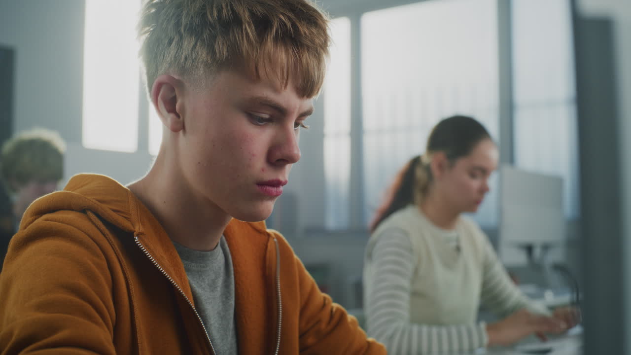 Male Student in Orange Hoodie Works on Computer Writing Code for Game Development Project