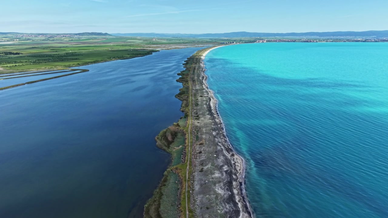 Kystlinje set fra oven viser sammensmeltning af blåt vand og land med klar himmel og grønne marker i det fjerne nær et kystområde.
