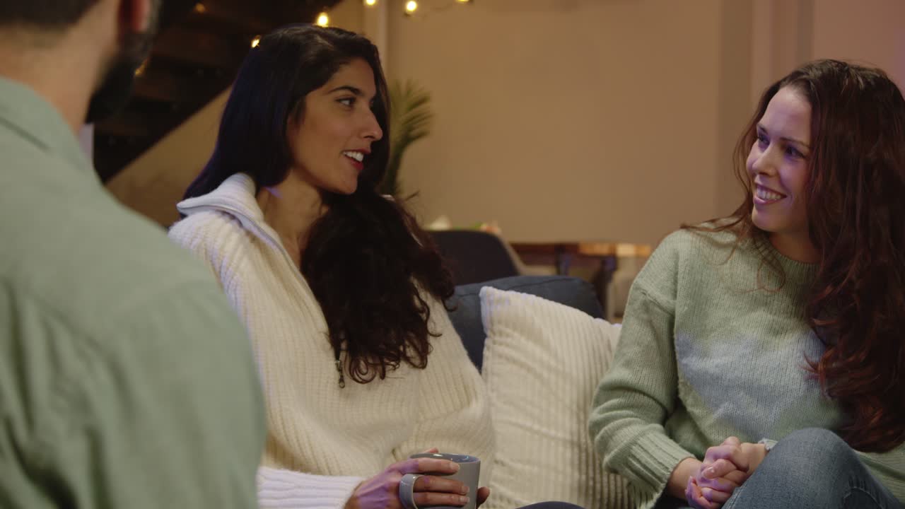 Relaxed Group Of Friends Sitting On Sofa At Home Or In Bar Or Coffee Shop Talking And Drinking Coffee Together