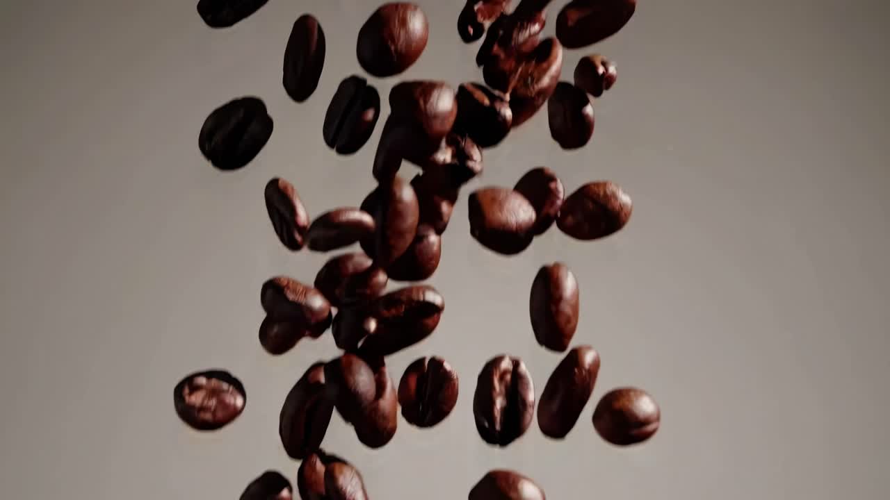 Video ravvicinato di chicchi di caffè che cadono a mezz'aria su uno sfondo neutro