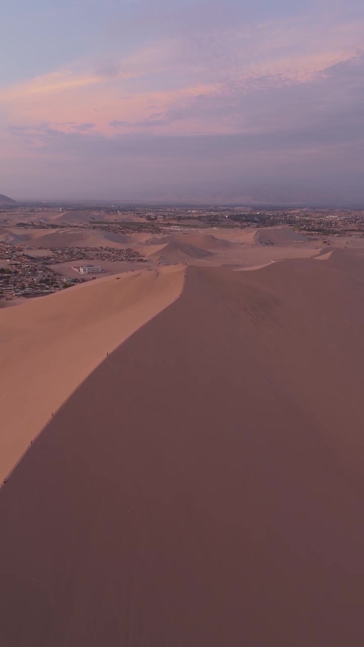 Ascesa aerea sopra un'imponente cresta di dune che domina la periferia del deserto al tramonto, ripresa verticale con drone.