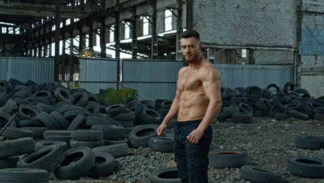 handsome muscular man posing outside. muscular man standing against old tyres background