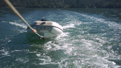 slowmo - inflatable boat being towed on rope behind boat on sea of new zealand