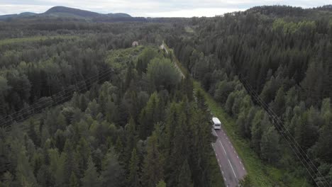 aerial wide shot of white camper van driving down road, gently rising up revealing lush, dense, dark green nordic forest full of coniferous trees