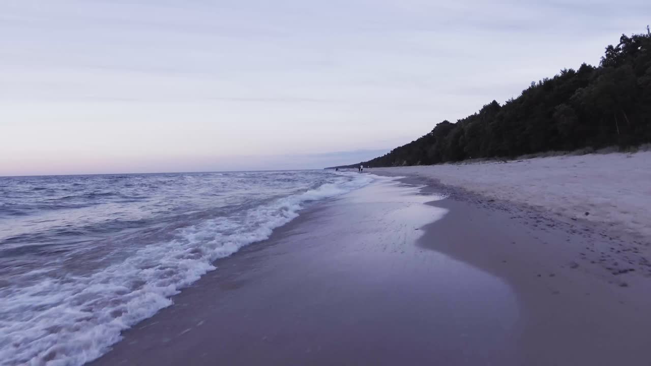 A smooth video on a summer evening on the beach.
The water creates small waves on the lovely beach.
You can also see unrecognizable people walking in the background.
