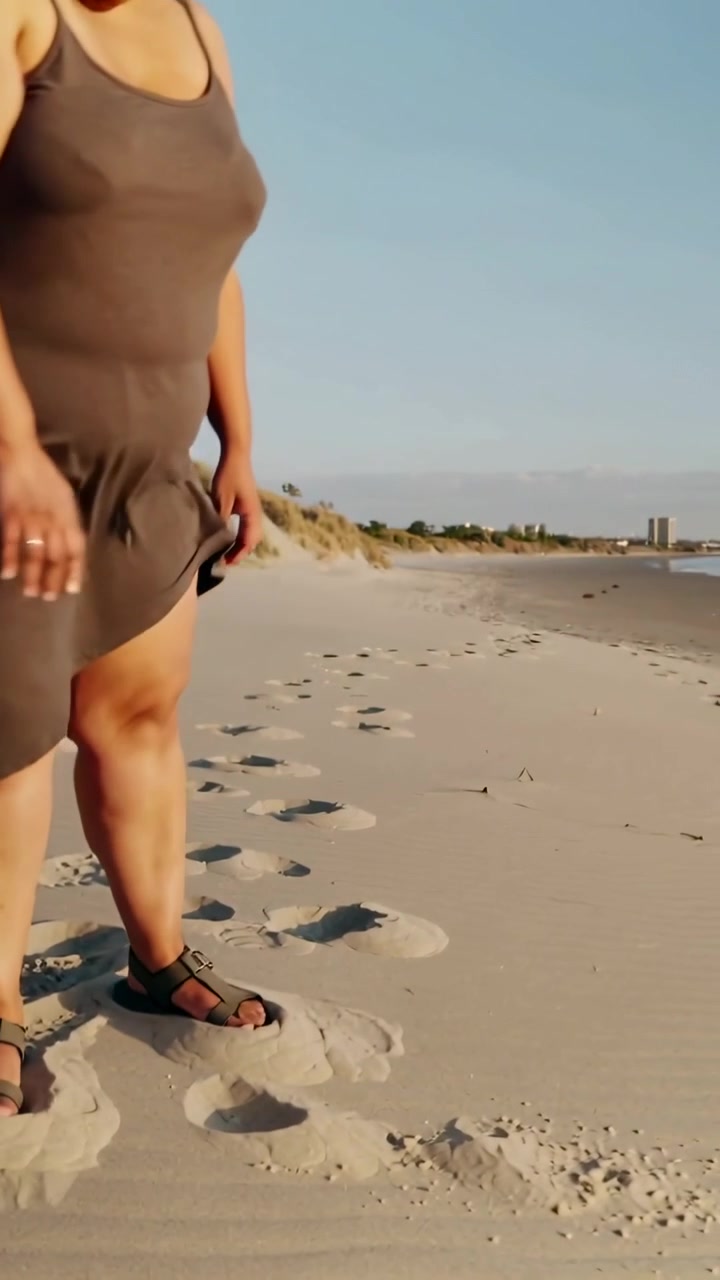 Video verticale: Donna accovacciata in abito che lascia cadere la sabbia camminando sulla spiaggia, creando disegni con il cellulare