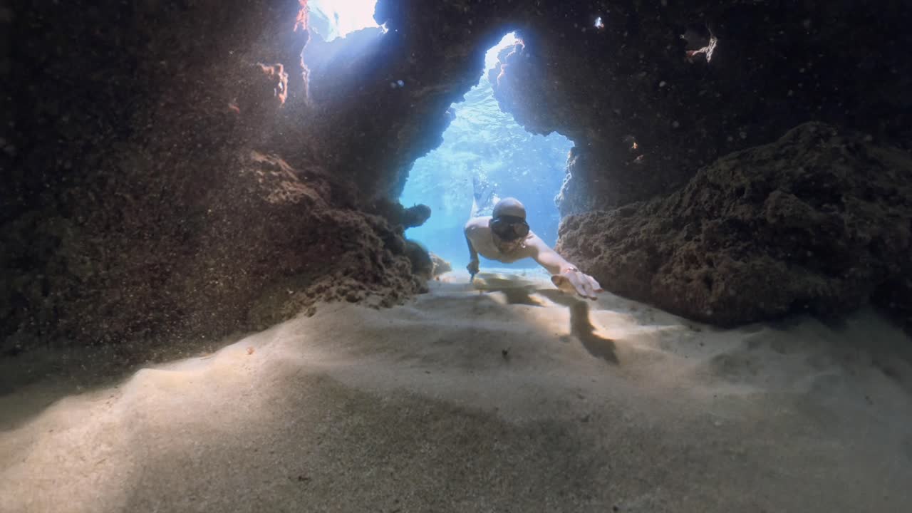 Man freediving and swimming through natural rock arch in clear turquoise water