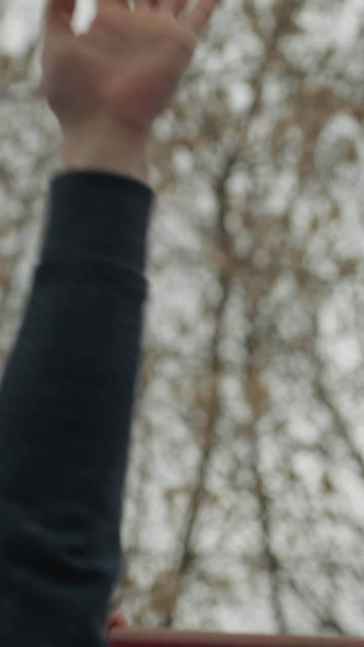 close up of a someone's hand holding a red iron bar as he moves over to the other iron bar, with bare tree seen above