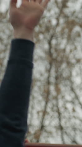 close up of a someone's hand holding a red iron bar as he moves over to the other iron bar, with bare tree seen above