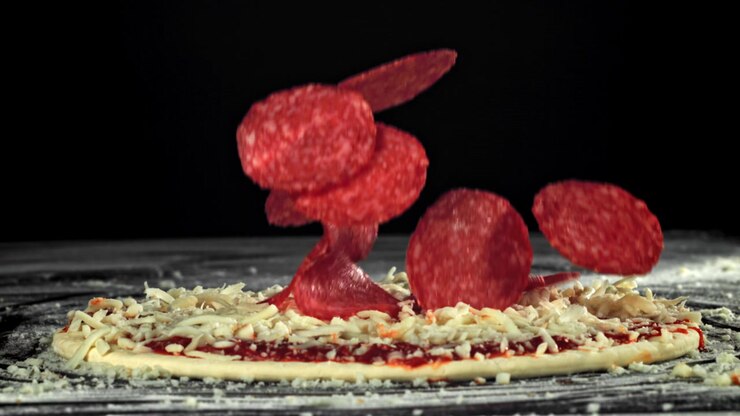 Fette di salame piccante che cadono al rallentatore su pizza cruda