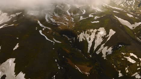 Aerial-landscape-view-over-a-waterfall-in-the-icelandic-mountains-with-melting-snow,-on-a-cloudy-and-foggy-day