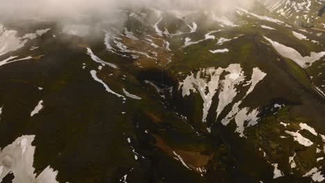 aerial landscape view over a waterfall in the icelandic mountains with melting snow, on a cloudy and foggy day
