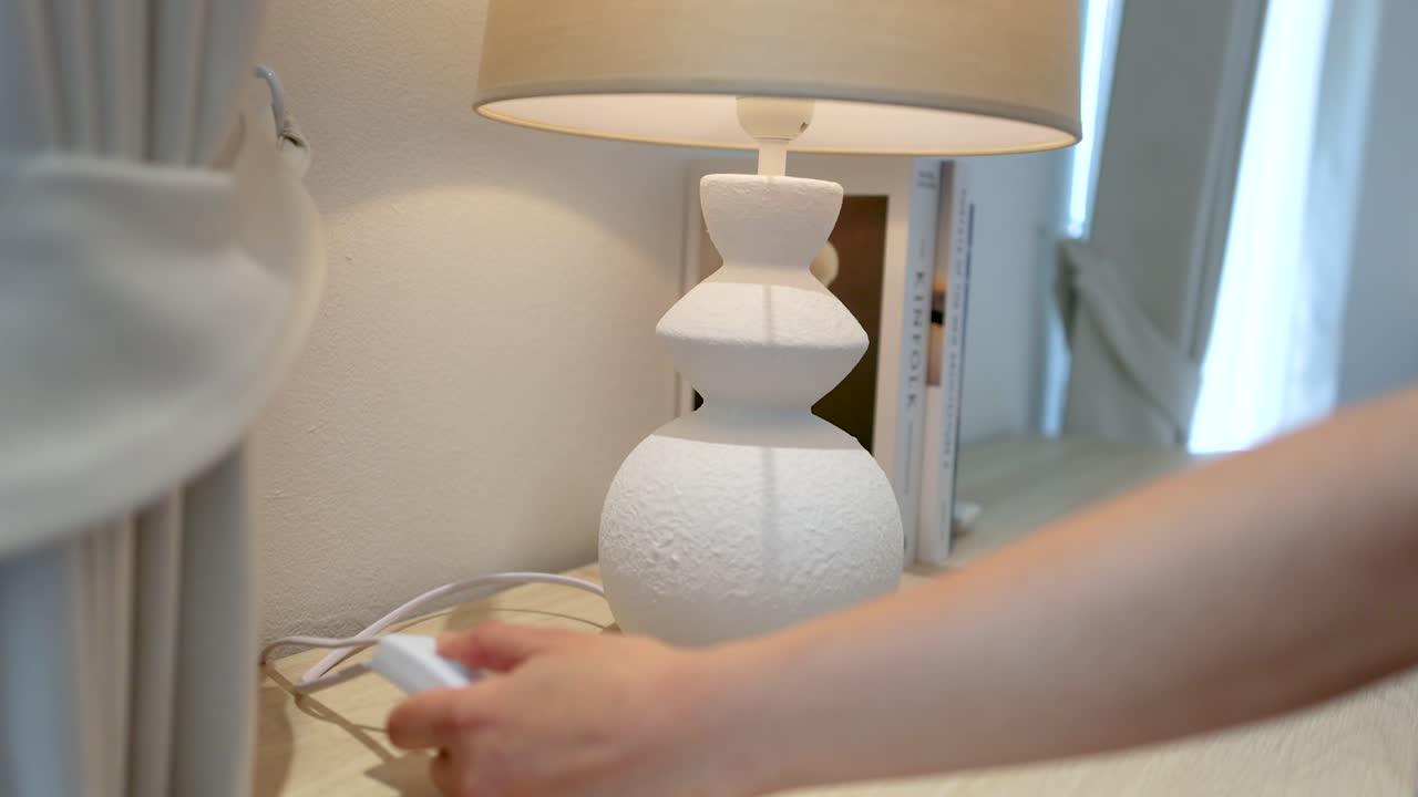 En hånd strekker seg ut for å klikke på en ledningsbryter, og slår av en hvit keramisk lampe