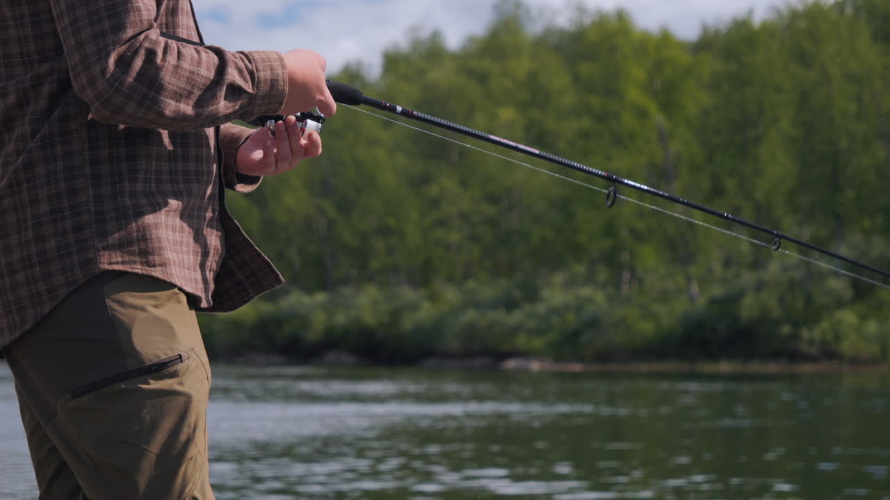 человек, ловящий рыбу на реке, близкий взгляд на руки, технику и кастинг.