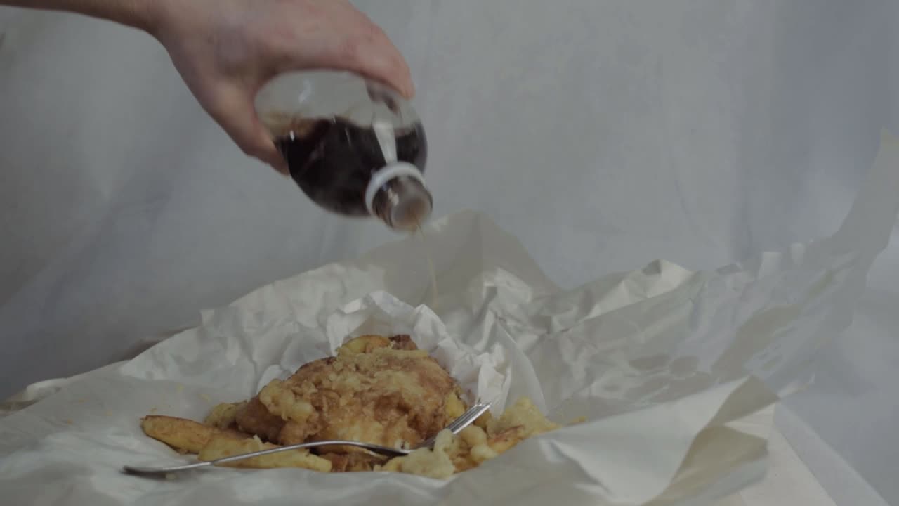 Hand pouring vinegar on fish and chips medium shot