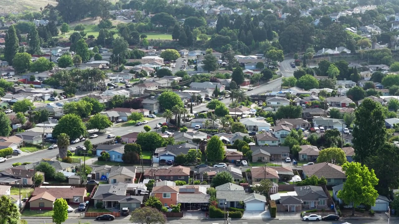 Bairro residencial de Vallejo com casas térreas estilo rancho, árvores maduras e ruas ladeadas por palmeiras, estendendo-se por um terreno plano em direção a colinas verdes e ondulantes. Califórnia, EUA. Vista aérea.