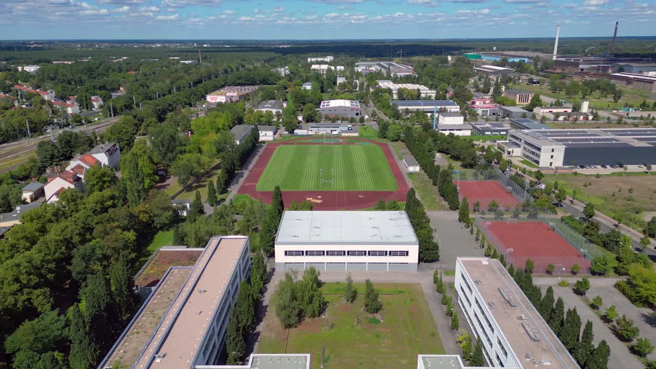 sports facilities at Hennigsdorf high school, including a soccer field, running track and other buildings in residential areas. Lovely aerial view flight fly reverse drone
