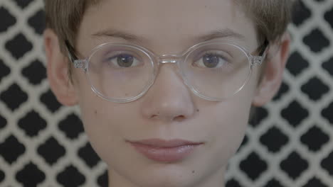 Cute-boy-wearing-glasses-and-sitting-in-a-designer-chair-smiles-a-subtle-smile-at-camera