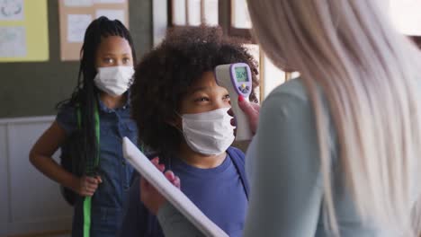 boy wearing face mask getting his temperature measured in class at school