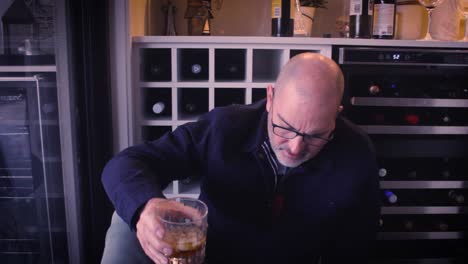 an angry middle aged man sits on the ground drinking a glass of alcohol