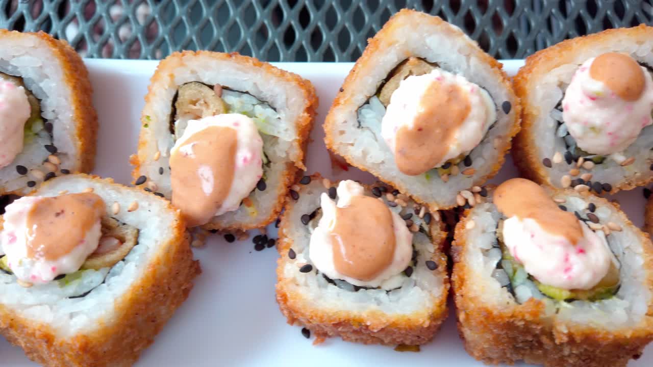 Top-down close-up of delicious fried sushi rolls garnished with creamy sauce and sesame seeds on a white plate.