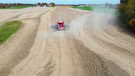 Farm-Combine-harvesting-soybeans-with-trailed-by-a-dust-cloud-on-a-Midwestern-farm,-aerial-drone