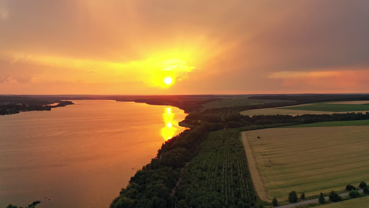 Beautiful river and green scenery in the evening with the setting sun. Amazing view of calm atmosphere of natural environment in rural place at orange sunset. Motion camera to right. Aerial view.