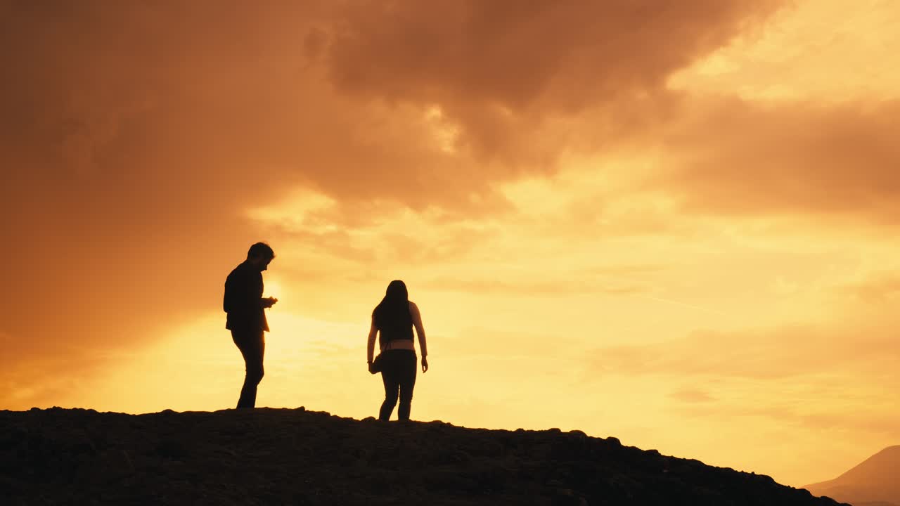 Silhouettes of young couple on mountain photograph orange yellow sunset
