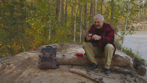 hombre alegre de mediana edad se está preparando para la pesca en la costa del río del bosque en un lugar ecológicamente limpio relajarse y pasatiempo