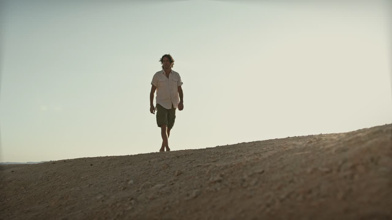 video cinematográfico de un hombre vestido con ropa de verano caminando por el desierto en un día extremadamente caluroso en la cumbre